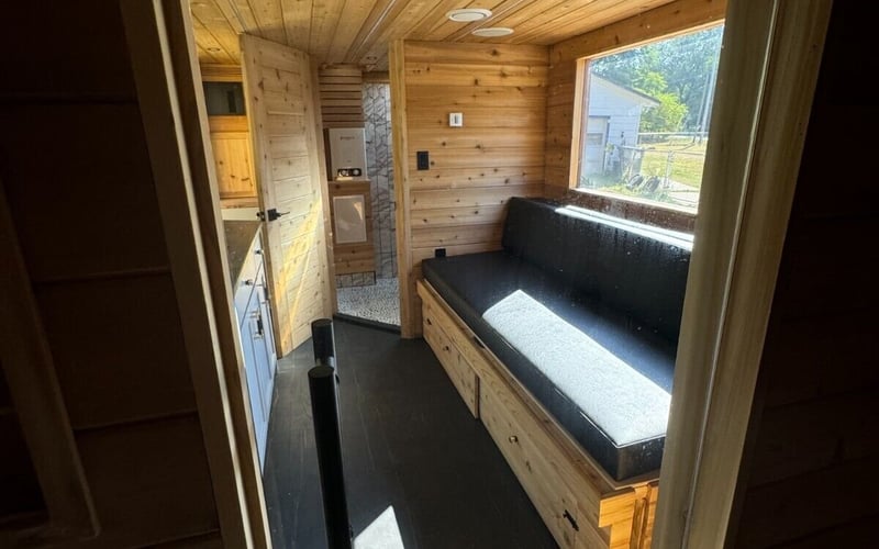 Wooden interior with black cushion bench, large window, ceiling vents, and door to restroom