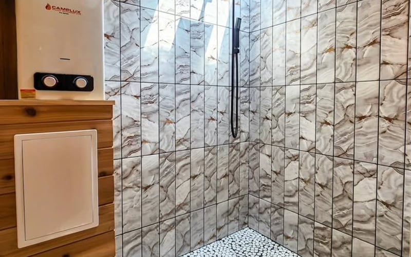 Marble tile shower with black rain shower head, skylight, and wooden ceiling