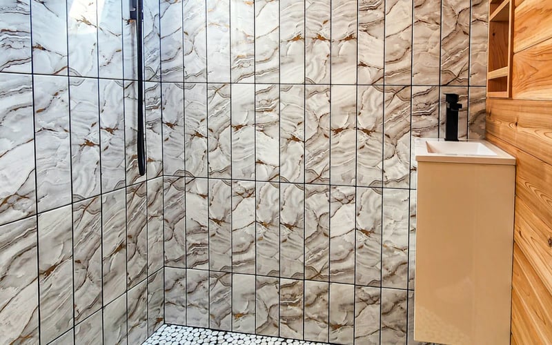 Marble tile shower with black piping, white vanity, pebble floor, and skylight