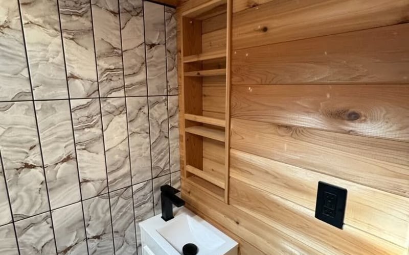 Bathroom corner with white sink, black faucet, wooden wall paneling, and marble tile